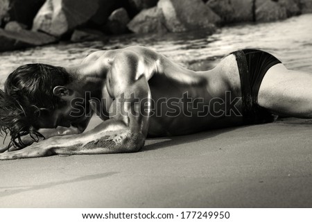 Fine art black and white sensual body portrait of a sexy muscular fit young man laying on beach