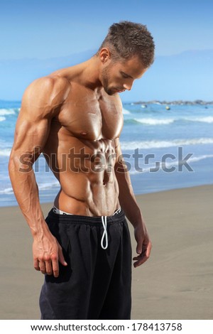 Muscular and fit young bodybuilder fitness male model on beach