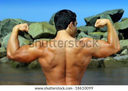 body builder flexing his back by the ocean with rocks in the background - full color photo -