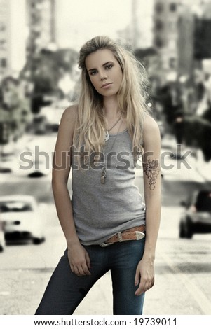 Textured (grain) photo of young female model in gray wife beater standing against vintage aged city background
