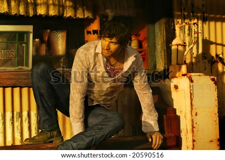 Horizontal full body fashion portrait of a young good looking male model in stylish white shirt against rustic background