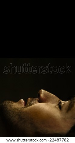 Dramatic close-up profile portrait of young man\'s face at the bottom of frame against black background and lots of top copy space