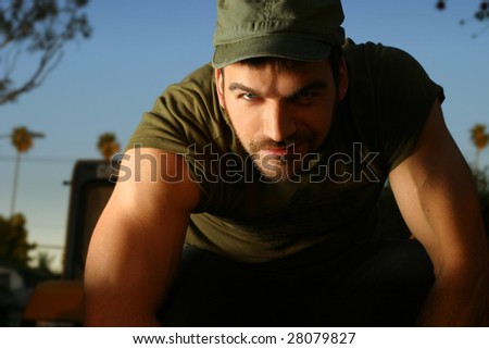 Portrait of a sexy young man in green cap and shirt outdoors
