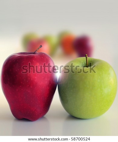 Abstract still life composition of two apples, one green, one red, side by side in front of blurred group of apples distant in the background