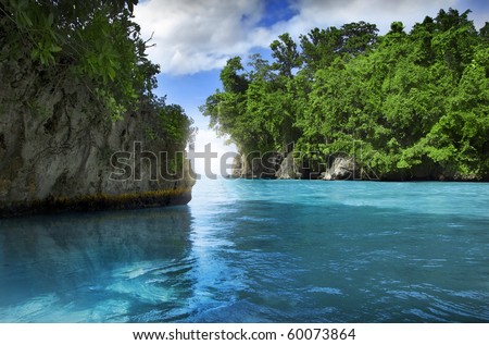 Beautiful secluded cove in the Caribbean featuring turquoise waters and blue sky framed by green vegetation and sun flare