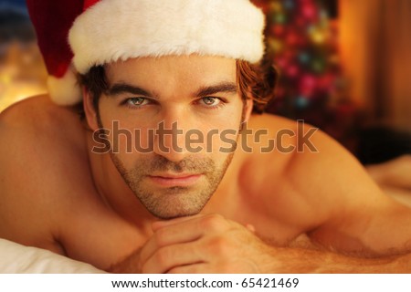 Young man bathed in warm light from fireplace wearing Santa cap