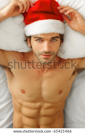 Sexy shirtless male model laying back in bed wearing Santa cap