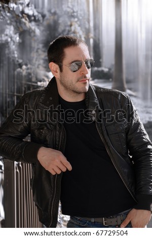 Sexy guy with attitude wearing leather jacket and sunglasses outdoors