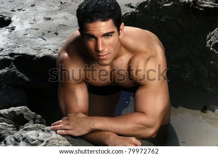 Attractive male muscular fitness model on the beach with rocks