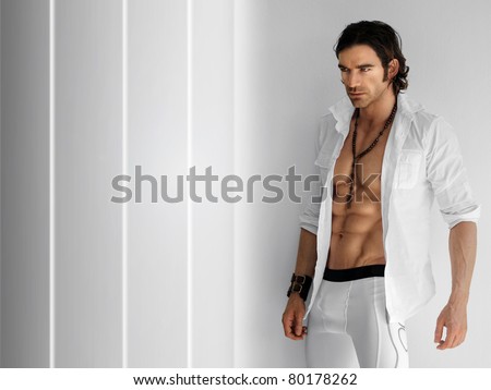 Portrait of a handsome fitness model wearing open crisp white shirt and white long boxer briefs against modern background