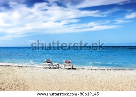 Two blue and white beach chairs on tropical white sand beach with bright blue sky