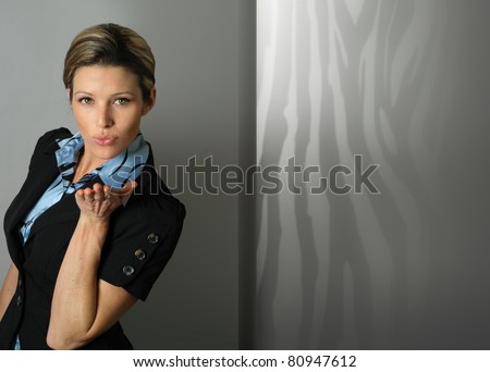Playful executive business woman with open palm blowing kiss in modern office setting