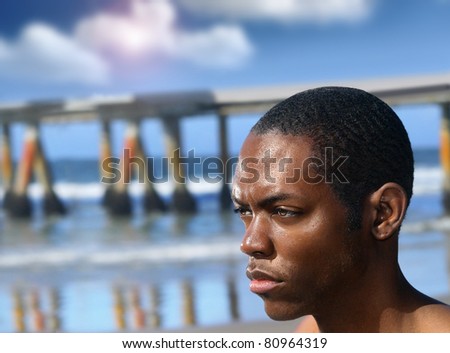 Portrait of a young serious man in profile outdoors with beach piers reflecting in ocean in background