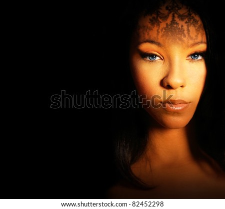 Fashion style portrait of a beautiful female model with exotic makeup and dark background with lots of copy space