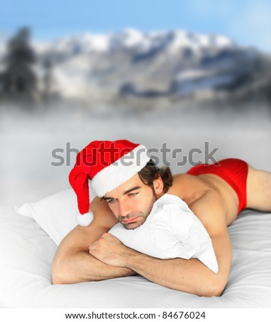 Hunky male santa laying in bed on pillow with winter snow background