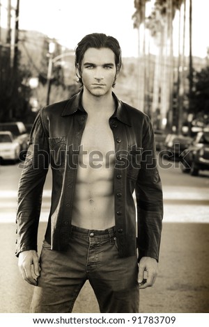 Sepia toned fashion portrait of an edgy male model wearing leather jacket and shirtless outdoors