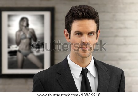 Portrait of a young elegant businessman in suit against neutral modern background with framed photo of sexy woman