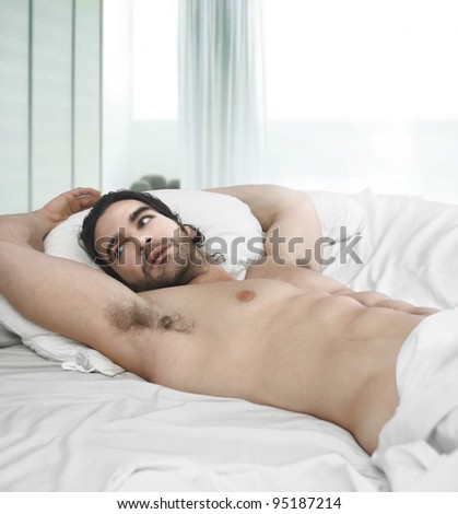 Portrait of a naked man in bed with window behind him