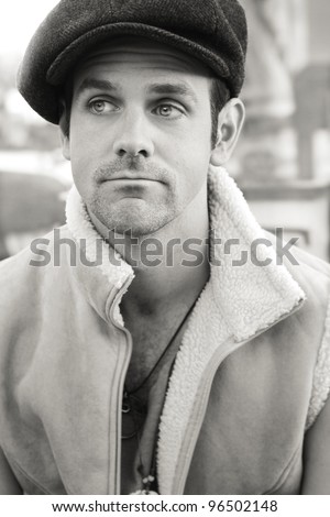 Portrait of a young man outdoors in sepia tones wearing hat and vest