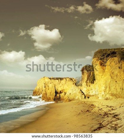 Ocean shoreline landscape with sand and cliffs in golden morning light and gray sky above