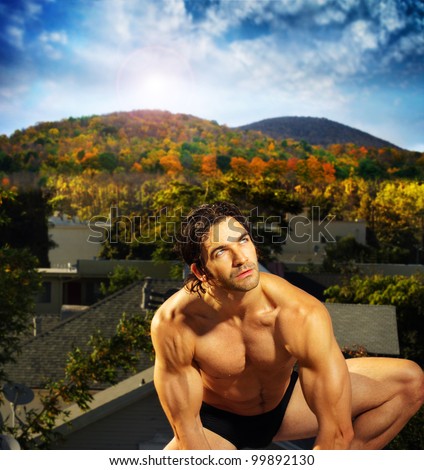 Outdoor portrait of a sexy shirtless male model crouching down against beautiful outdoor setting