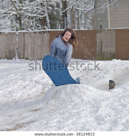 Teen girl jumping off of a snow bank on a sled on a winter day after a huge snow storm.