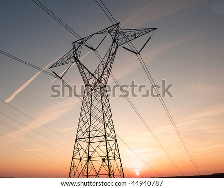 Electric power pylon and wires silhouetted by ab colorful sunset.