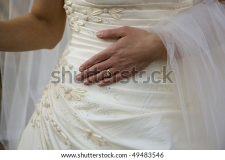 Bride with her new ring.  Engagement and wedding band on the finger of a bride in her dress and veil, resting on her abdomen.