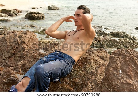 Muscular young man laying on the rocks on the beach running his fingers through his wet hair.