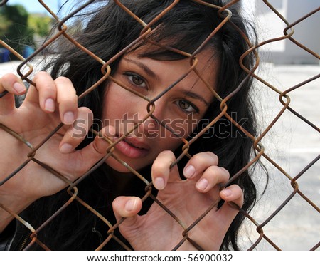 Beautiful brunette woman grasping onto the links of a chain fence trapped in the city.