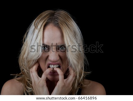 Angry woman biting her nails in studio on a black background with room for text.