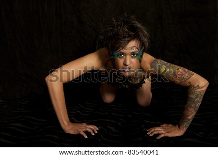 Retro image of a beautiful woman with tattoos crouching down on black background.