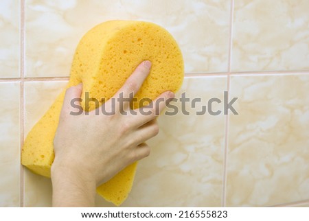 Hand with yellow sponge wipes wall of tile