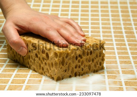 Hand with yellow sponge with foam on the tile
