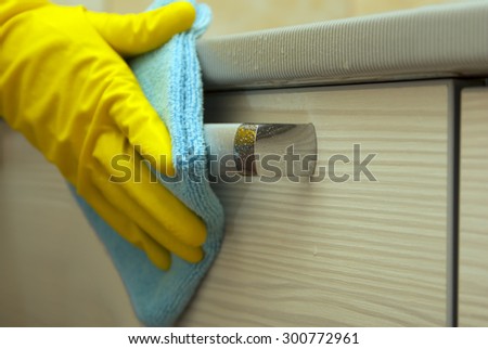 hand in yellow glove with blue cloth on the silver handle of furniture wipes water droplets