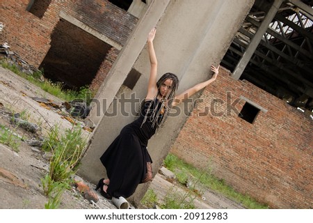 fashionable girl in black dress alongside of column on the dirty industrial place