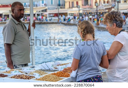 CHANIA, CRETE, GREECE - AUGUST 18, 2013: Young girl and old woman buy nuts from street seller at Chania old town port. Chania is one of the most popular towns on Crete island.