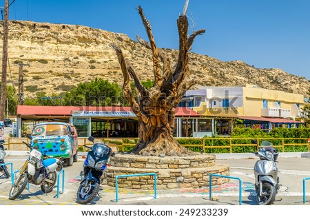 MATALA, CRETE, GREECE - AUGUST 20, 2013: Famous tree, hippie bus and motorcycles  in Matala center on Crete island