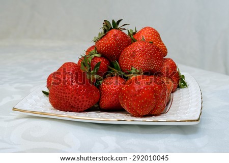 Small white plate, filled with succulent juicy fresh ripe red strawberries on a white textured table