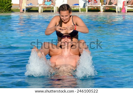 Two adults having fun in pool, man throws woman from his shoulders