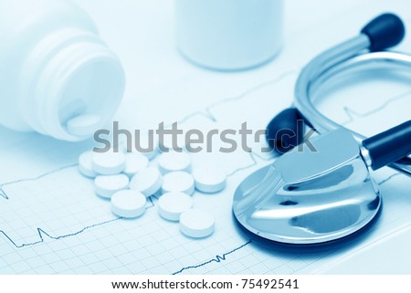 Medical still-life with cardiogram, stethoscope and spilled tablets (blue toned)