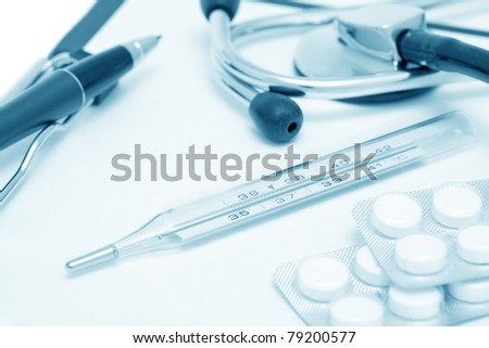 Medical still-life with stethoscope, clipboard, pen, thermometer and tablets. Blue toned