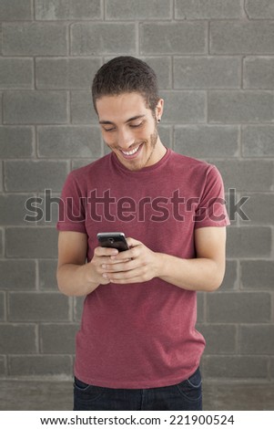 Happy smiling young man portrait touching a mobile screen over brick background