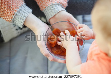 baby taking dried apricots from the glass plate. Healthy vegan food.