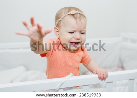 crying baby girl standing in the infant bed. She is having teeth pain