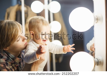 happy baby wants to touch light bulb at makeup mirror