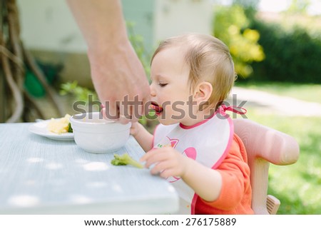 Baby girl eating her lunch in the garden outside in summer
