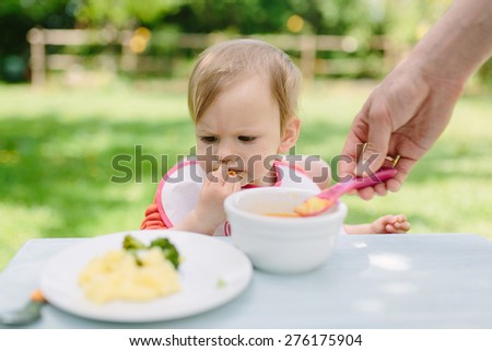 Baby girl eating her lunch in the garden outside in summer