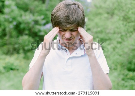 Young man having a head pain and puts his hands over the head. He is stressed