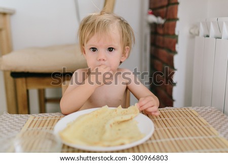 Cute baby eating a pancake sitting by a small wooden table